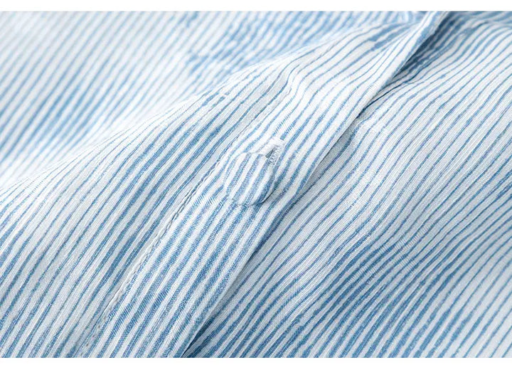Close-up of light blue and white pinstripe fabric on a dress, showing a fabric-covered button and subtle texture. This detail highlights the delicate material and construction.