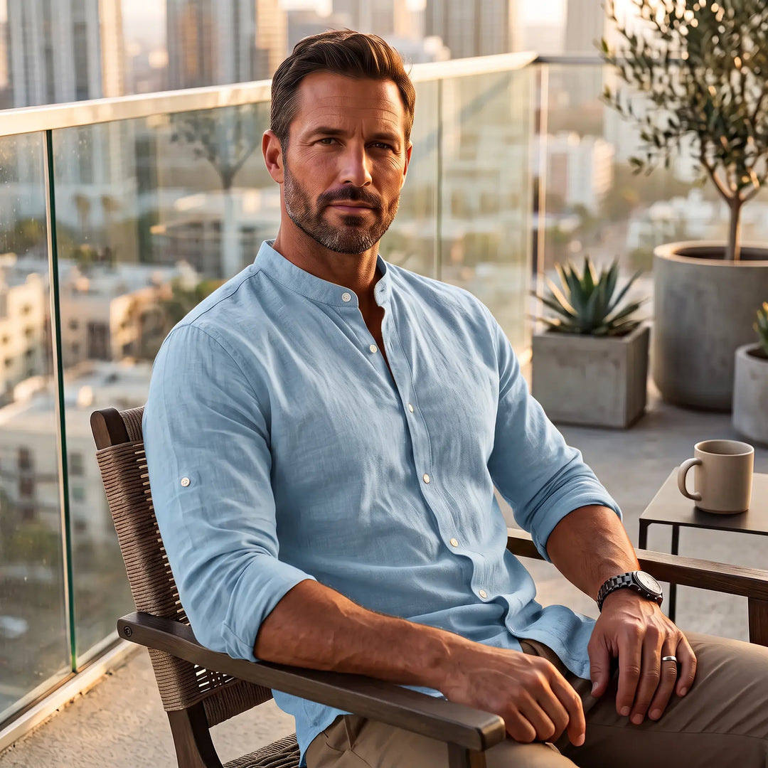 Man wearing a light blue long-sleeve linen-blend shirt with a Mandarin collar, seated on a balcony with a city view.