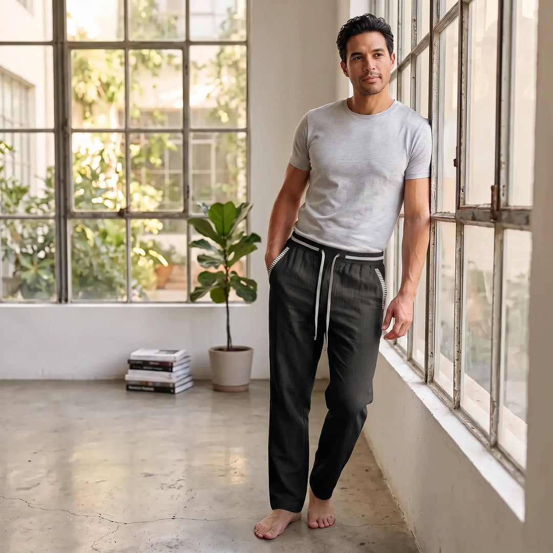 Man wearing Zylath classic black linen blend straight-leg trousers with a striped elasticated waistband and pocket trim, leaning against a window.