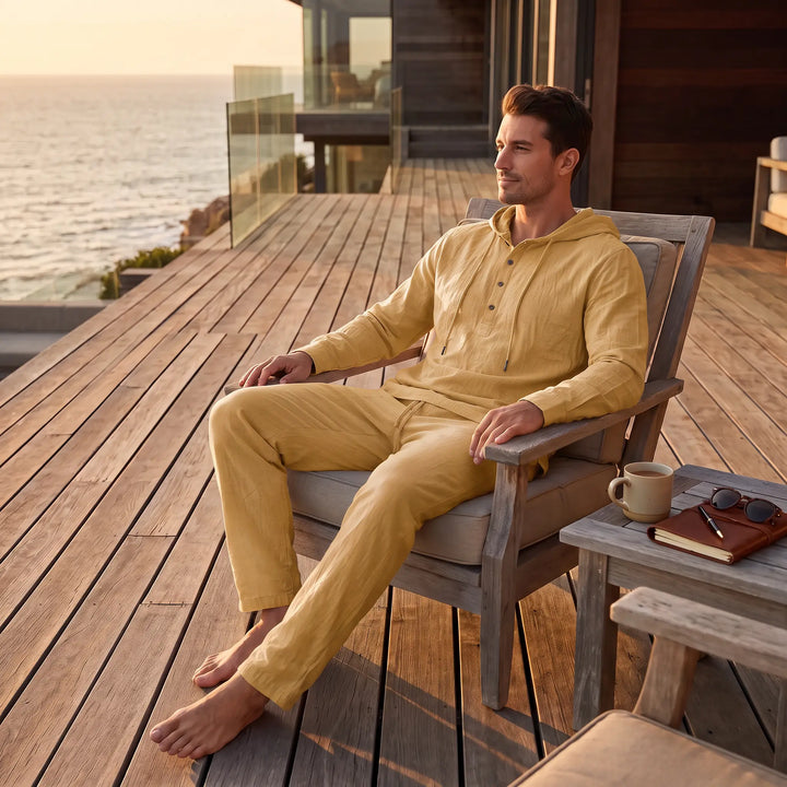 Man wearing a goldenrod linen blend loungewear set, featuring a hooded henley top and straight-leg trousers, relaxing on a wooden deck overlooking the ocean.