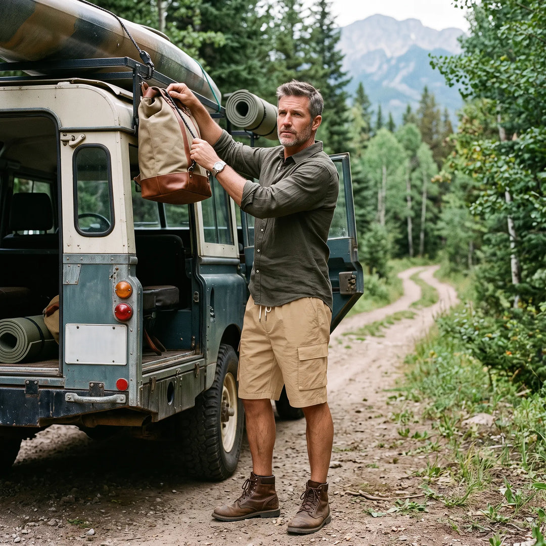 Man wearing khaki relaxed-fit men's cargo shorts with a drawstring waist and bellowed pockets, standing next to an off-road vehicle in a scenic mountain landscape. Lifestyle shot showcasing durability and outdoor readiness.
