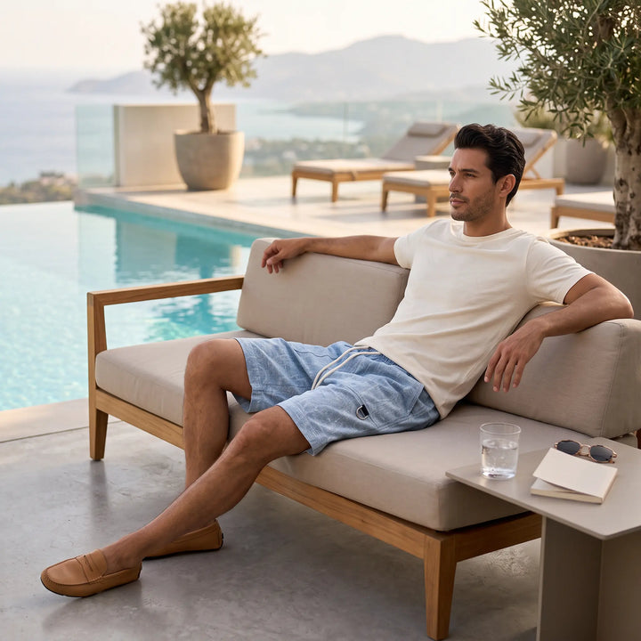 Man wearing light blue textured shorts with a rope drawstring and a D-ring tab cargo pocket, relaxing on an outdoor sofa by a pool.