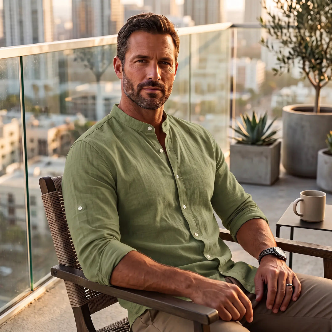 Man wearing a relaxed fit, olive green long sleeve linen blend shirt with a Mandarin collar, seated on a balcony.