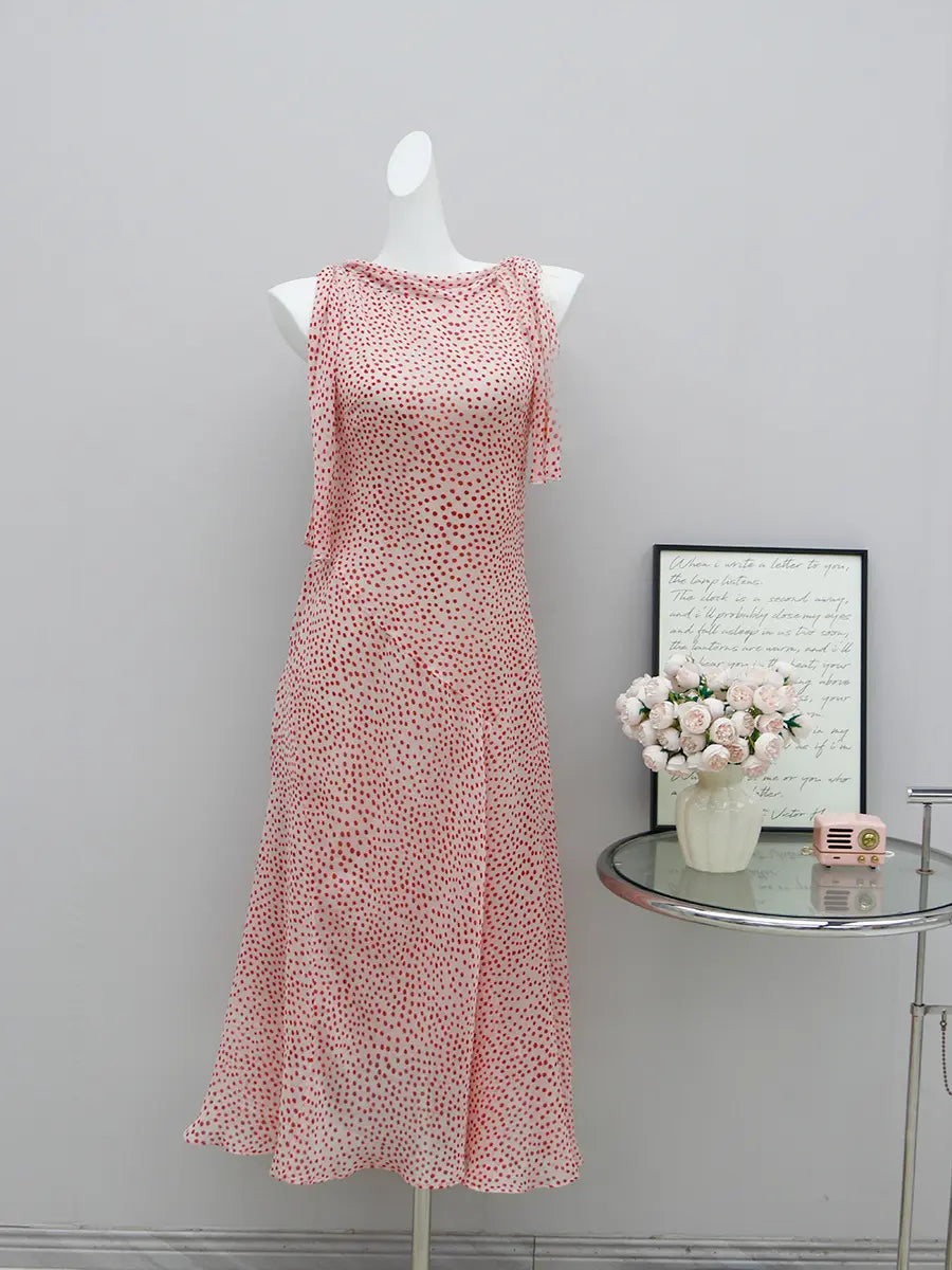 Elegant light pink midi dress with red polka dots, featuring a draped cowl neckline and sleeveless design on a mannequin.