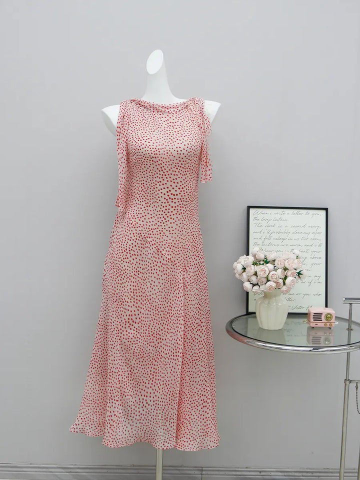 Elegant light pink midi dress with red polka dots, featuring a draped cowl neckline and sleeveless design on a mannequin.