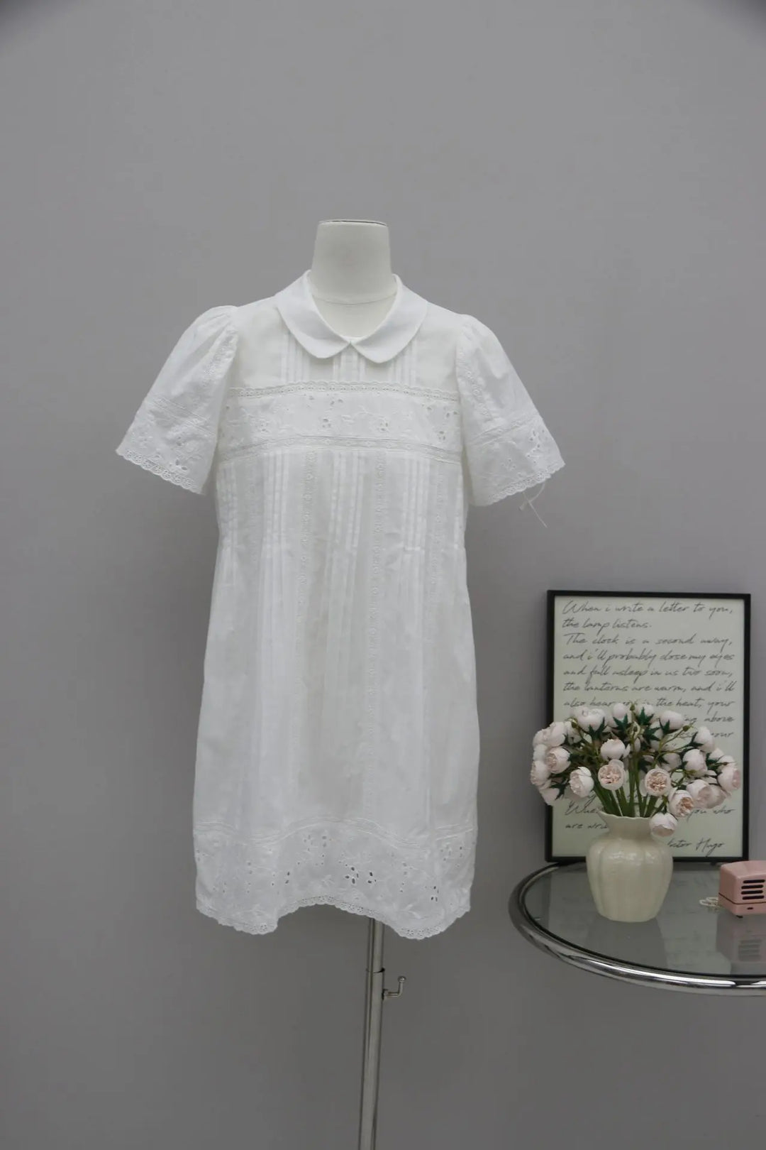 White cotton-blend A-line dress with Peter Pan collar, short puff sleeves, delicate floral embroidery, and lace trim, displayed on a mannequin.