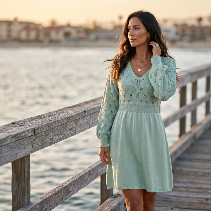 Model strolls on a wooden pier at sunset, wearing a muted mint V-neck midi knit dress featuring an intricate fish-scale pattern on the yoke and sleeves.