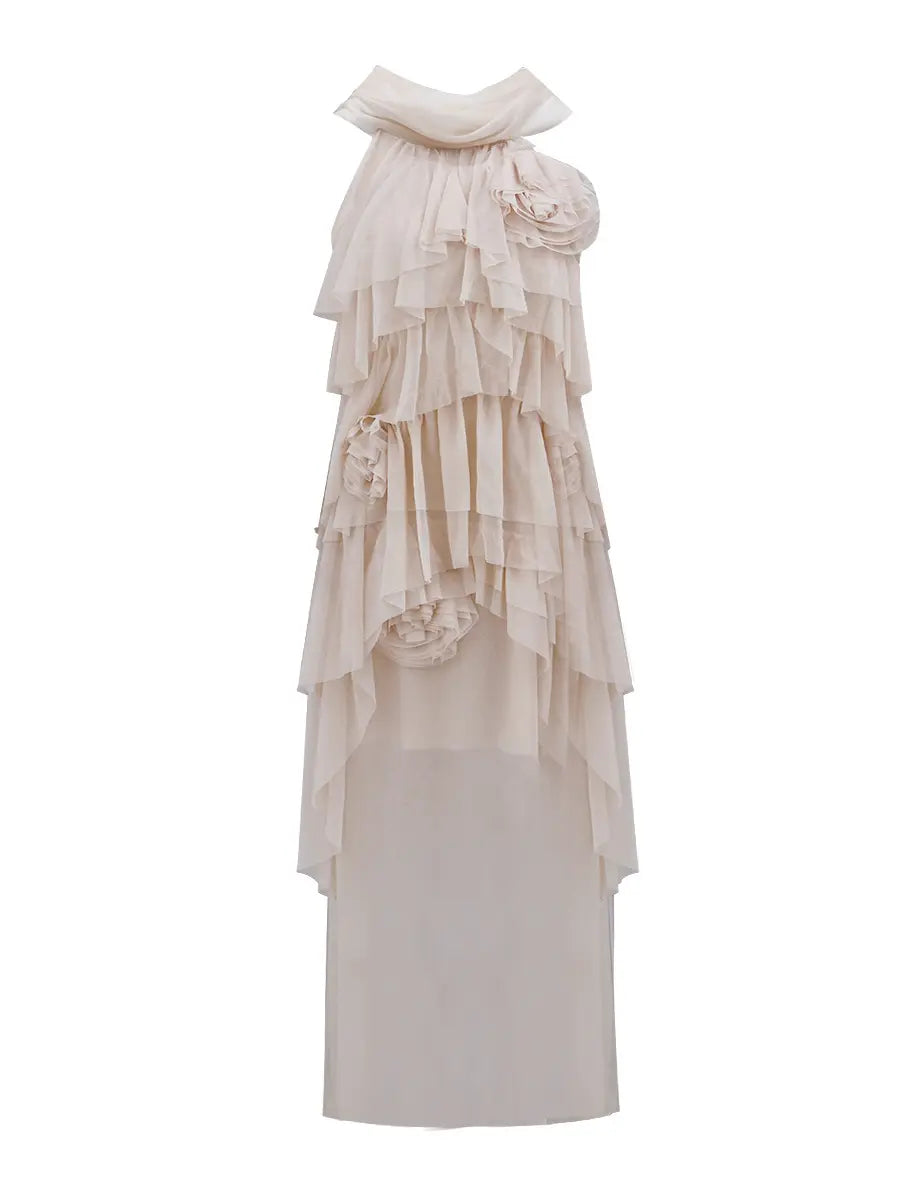 Ethereal nude layered ruffle maxi dress by Zynka, featuring a draped asymmetrical neckline, fabric roses, and cascading sheer tiers. This sleeveless gown has an uneven flowing hem and is presented on a white background.