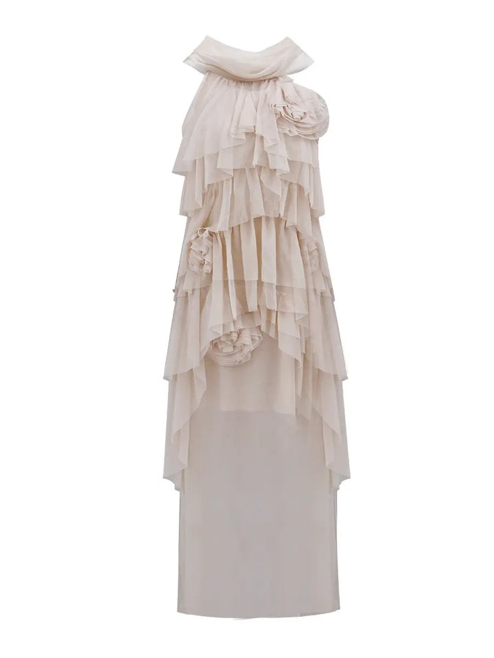 Ethereal nude layered ruffle maxi dress by Zynka, featuring a draped asymmetrical neckline, fabric roses, and cascading sheer tiers. This sleeveless gown has an uneven flowing hem and is presented on a white background.