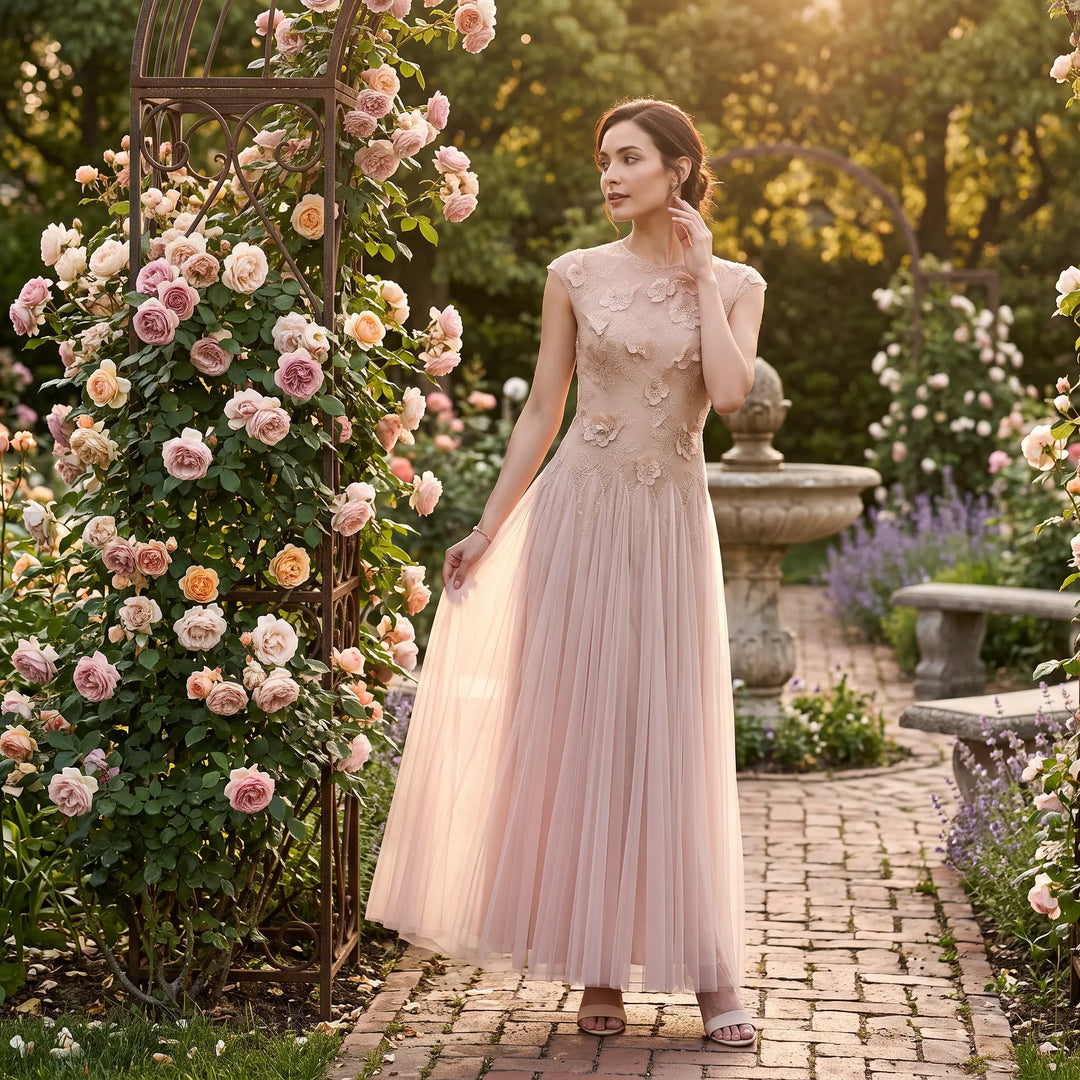 Elegant blush pink floor-length tulle evening gown with cap sleeves and intricate floral embroidery, showcased by a model in a romantic garden setting at golden hour.